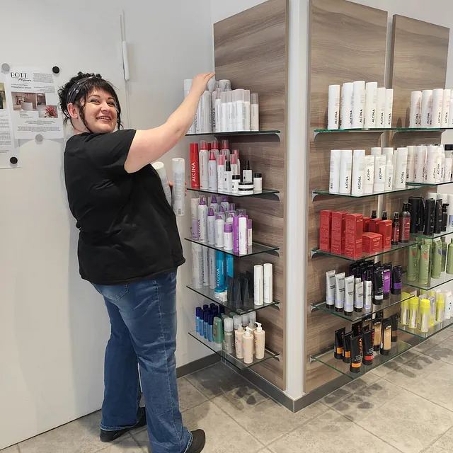 Eine Frau steht vor einem Regal mit Haarpflegeprodukten in einem Friseursalon. 
