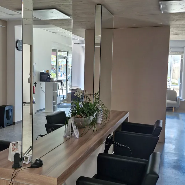 Ein Friseursalon mit einem großen Spiegel und mehreren Stühlen für Kunden. 