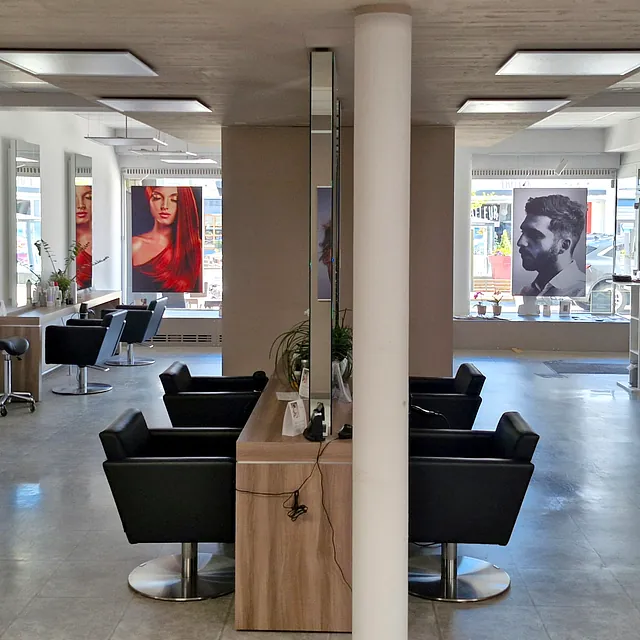 Innenansicht eines Friseursalons mit Stühlen und Spiegeln in der Raummitte.