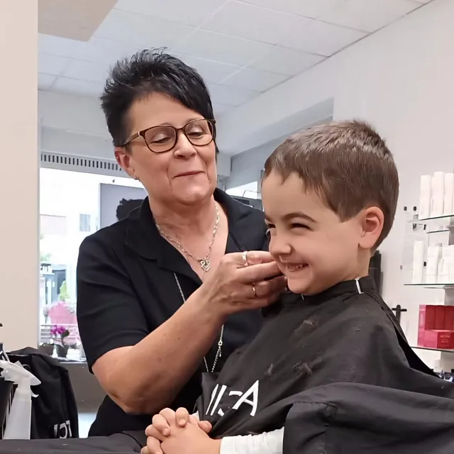 Eine Frau schneidet einem kleinen Jungen die Haare in einem Friseursalon. 