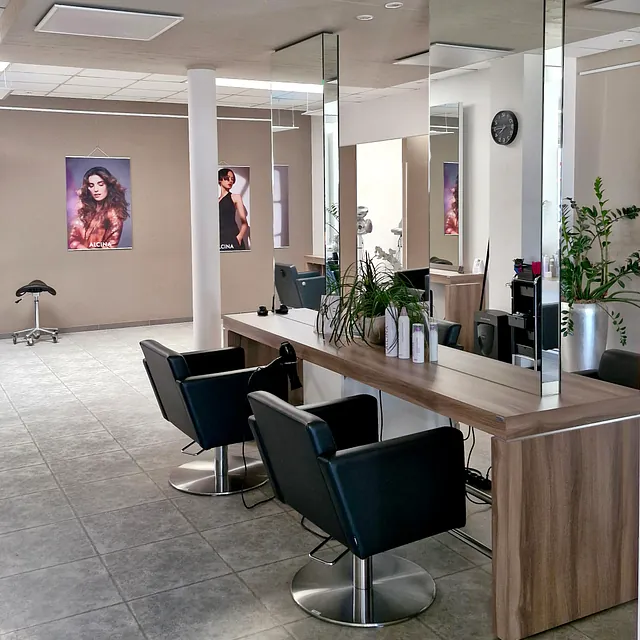 Innenansicht eines Friseursalons mit mehreren Stühlen und großen Spiegeln.